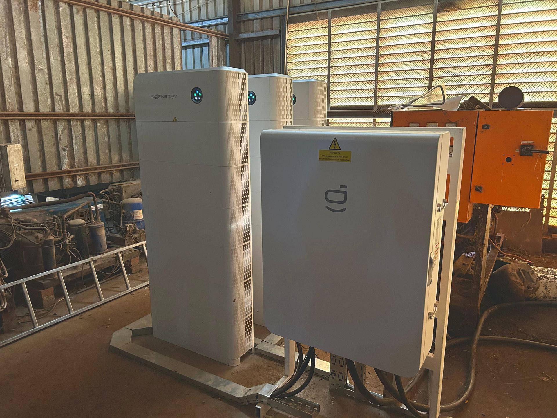 Angled view of the SigenStor gateway/inverter cabinet with floor conduits beside Sigenergy stacks at DB Dairy.