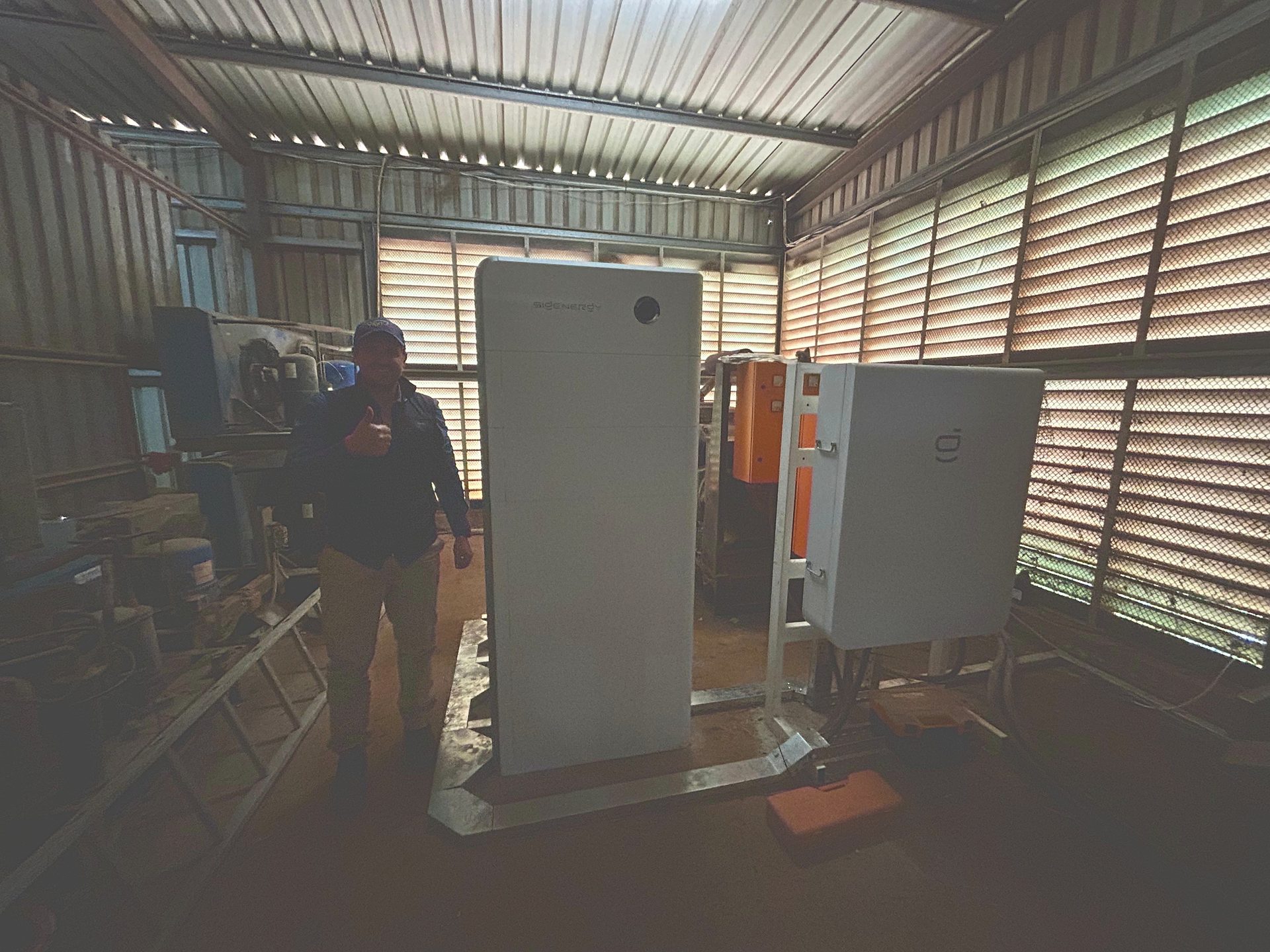 Install team member giving a thumbs-up beside a Sigenergy SigenStor stack and gateway cabinet after the DB Dairy hybrid install.